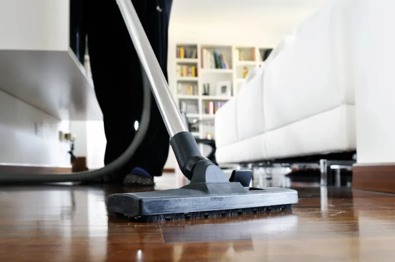 Gebäudereinigung mit Staubsauger auf Holzboden in modernem Wohnzimmer